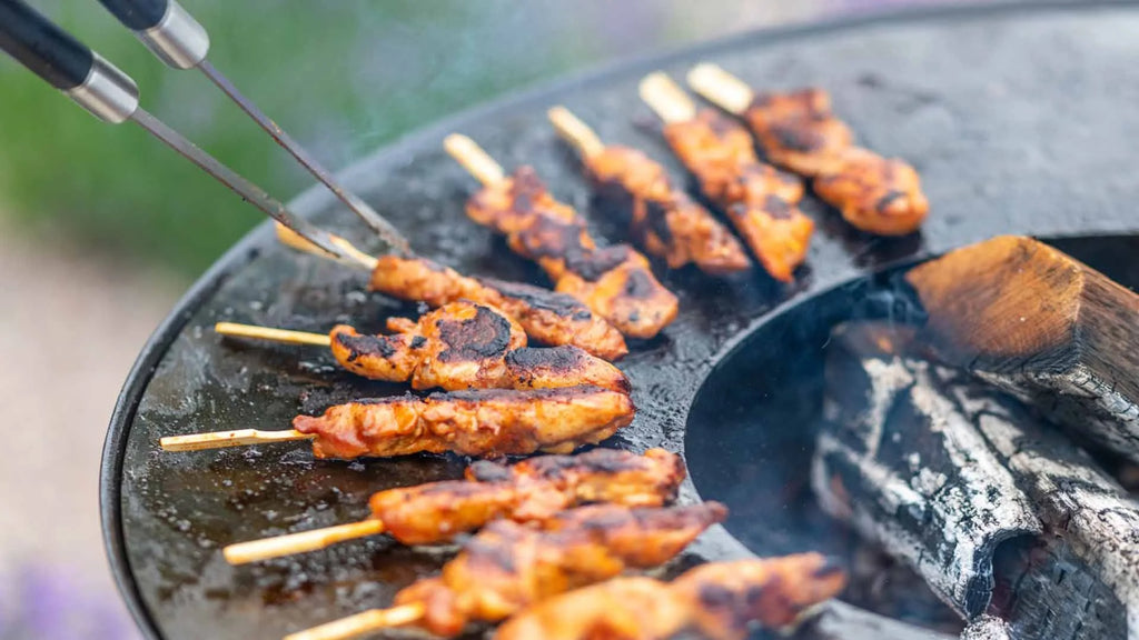 Brochettes de poulet grillé aux bords carbonisés et à la glaçure lustrée et savoureuse qui crépitent sur un gril en fonte noire au-dessus de braises rougeoyantes.