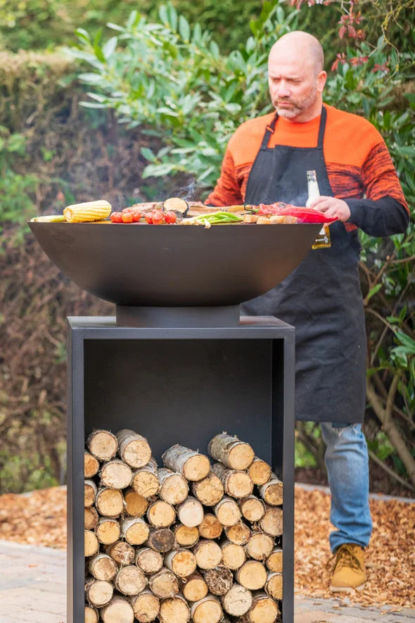 Foyer de feu noir en forme de bol avec une base de rangement pour bûches assortie