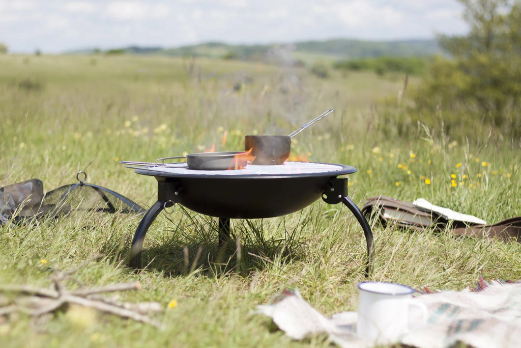 Grille de cuisson pour feu de camp en métal noir avec une petite casserole posée dessus