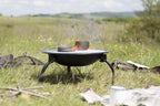 Grille de cuisson pour feu de camp en métal noir avec une petite casserole posée dessus