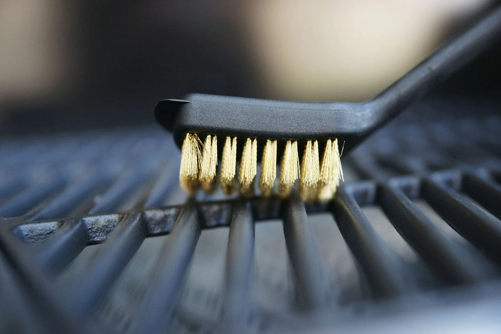 Brosse à gril en acier inoxydable avec manche noir et poils dorés, conçue pour nettoyer les grilles.