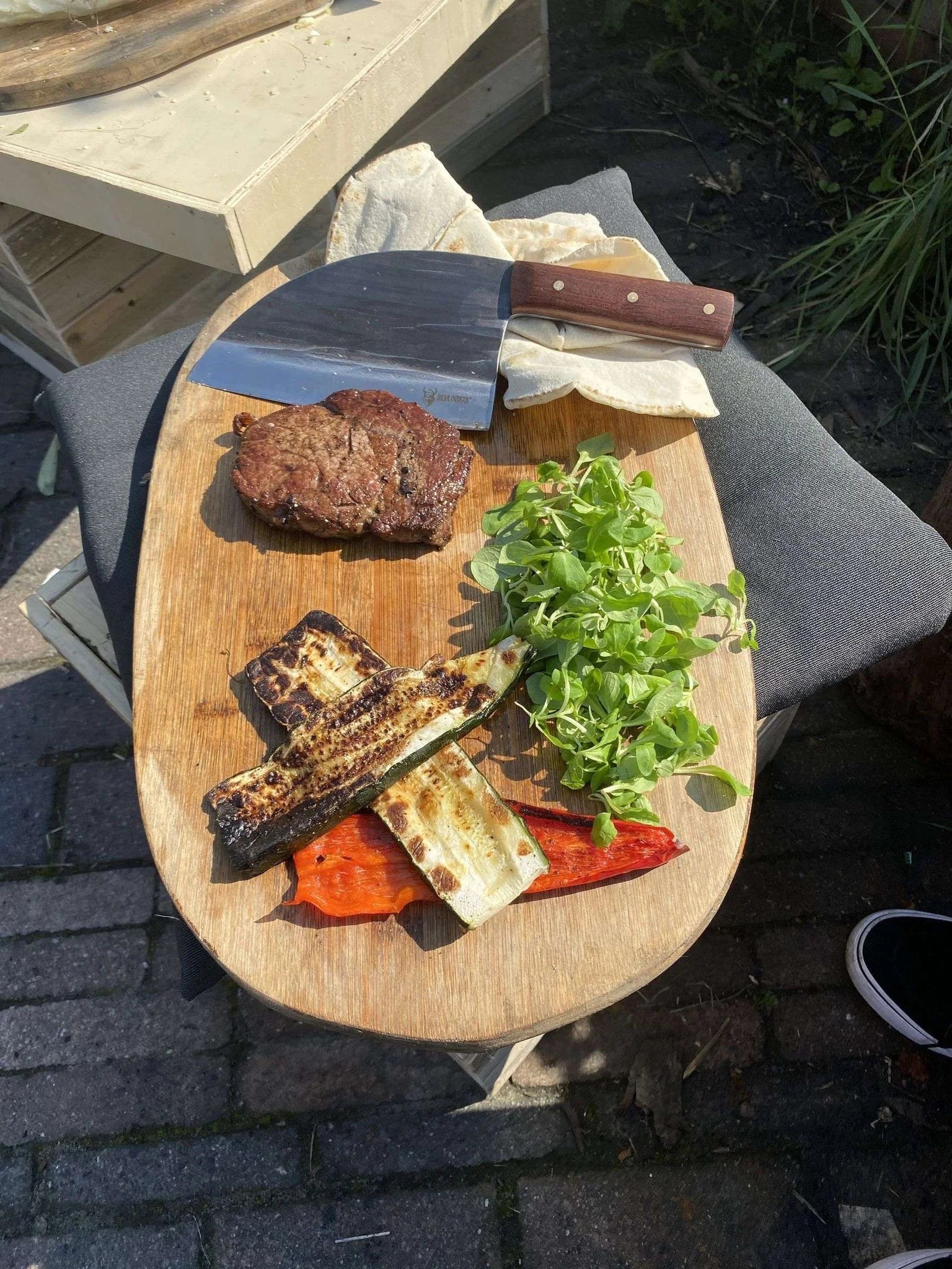 Planche à découper en bois avec légumes et viande grillés, manche de couteau en bois brun.