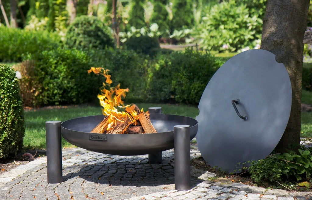 Foyer de feu noir avec pieds en métal et couvercle, utilisation extérieure.