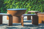 Foyer en acier Corten avec bancs courbés dans un cadre de jardin.