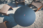 Table ronde extérieure noire avec accents en cuir tressé et un design minimaliste.