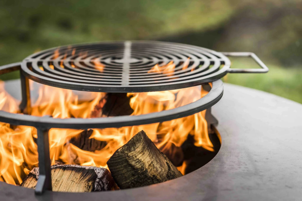Foyer de feu en métal noir avec grille circulaire et bûches en train de brûler à l’intérieur