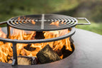 Foyer de feu en métal noir avec grille circulaire et bûches en train de brûler à l’intérieur