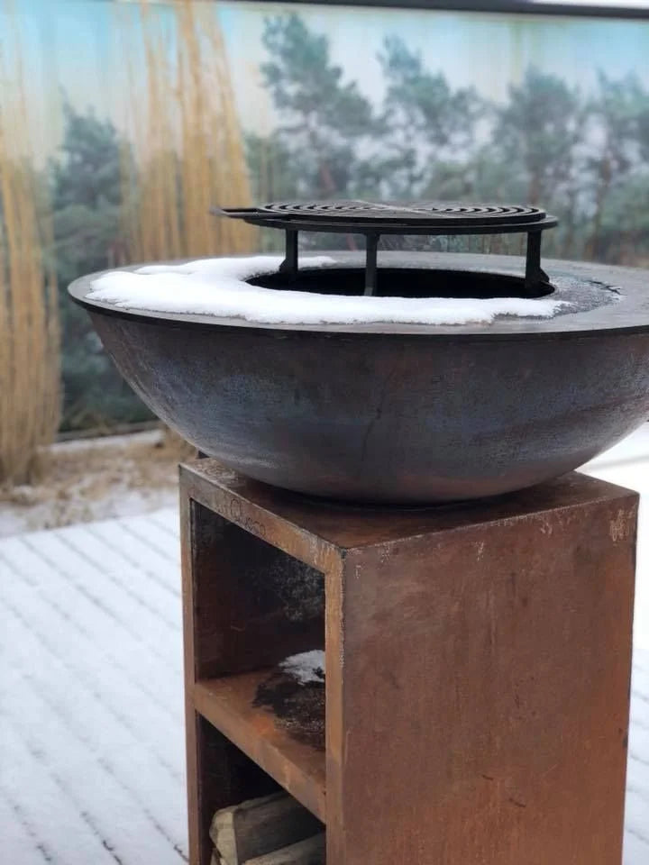 Bol en acier rouillé avec une grille en fonte noire reposant sur un support en bois usé.