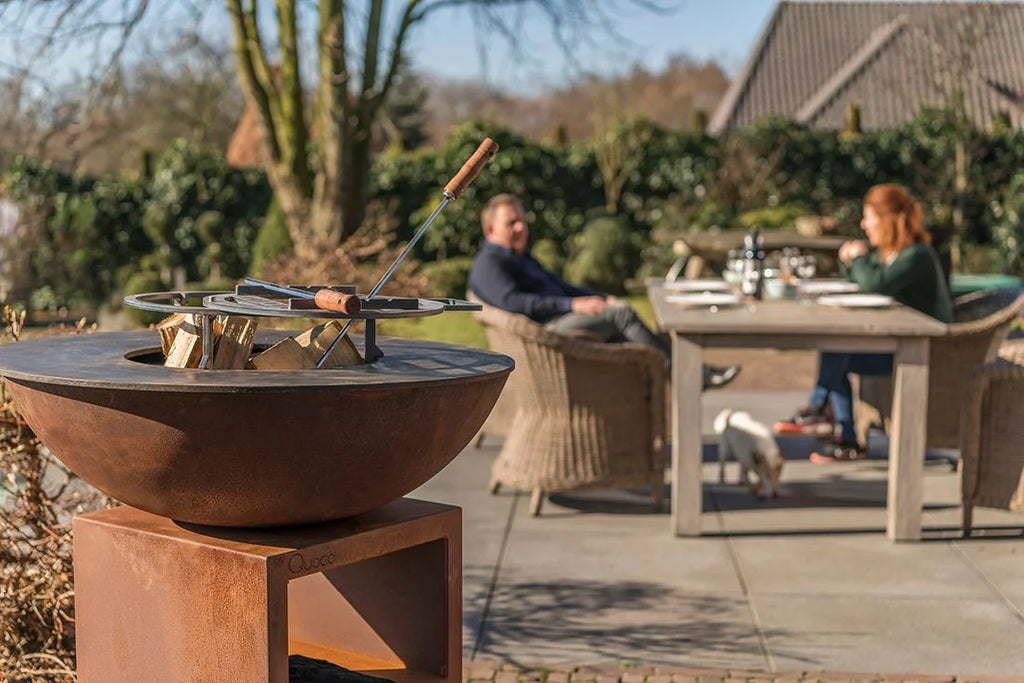 Bol en acier rouillé pour foyer avec outils à manche en bois reposant sur son bord.