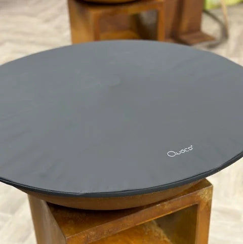 Tapis de table circulaire gris foncé avec une surface texturée subtile et le logo de la marque « quocco » brodé en blanc près du centre.