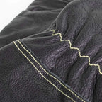 Gant en cuir noir avec coutures jaunes et surface texturée.