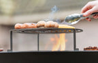 Grille cuisson acier ronde Ø80 cm plancha Onyx 80 avec saucisses et champignons sur flammes