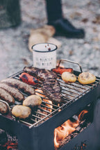 Barbecue portable en métal noir avec flamme ouverte et divers aliments en train de cuire dessus.
