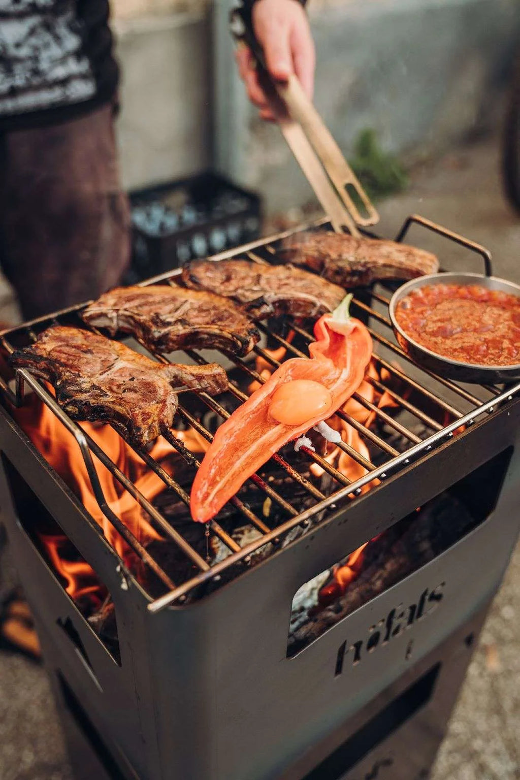 Gril tribus en acier inoxydable avec pinces en bois et récipient de sauce rouge.
