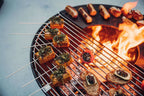 Gril à barbecue avec des légumes et de la viande embrochés, flammes visibles en dessous.