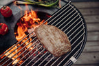 Barbecue au charbon avec un grand steak assaisonné sur la grille.