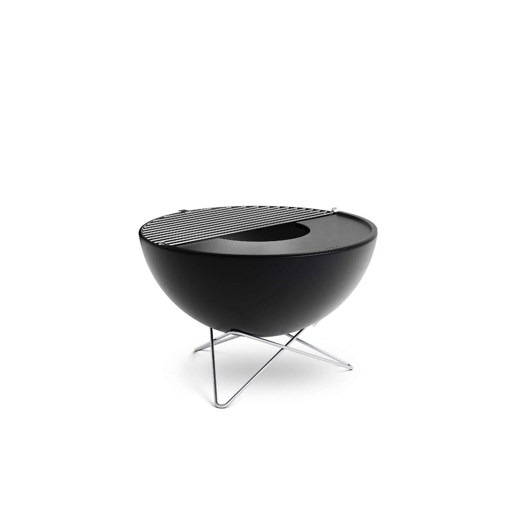 Foyer de feu moderne noir avec dessus pour gril et pieds trépied, probablement d’une marque contemporaine pour l’extérieur.
