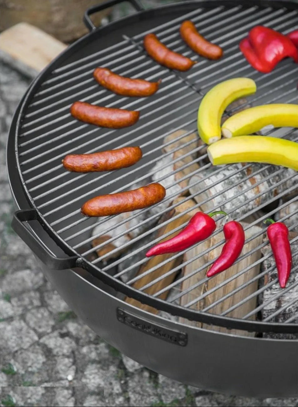 Barbecue au charbon avec des saucisses, des bananes et des poivrons rouges sur la grille.