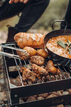 Barbecue au charbon avec des ailes de poulet et des pommes de terre sur la grille, accompagnée d’une casserole de soupe.