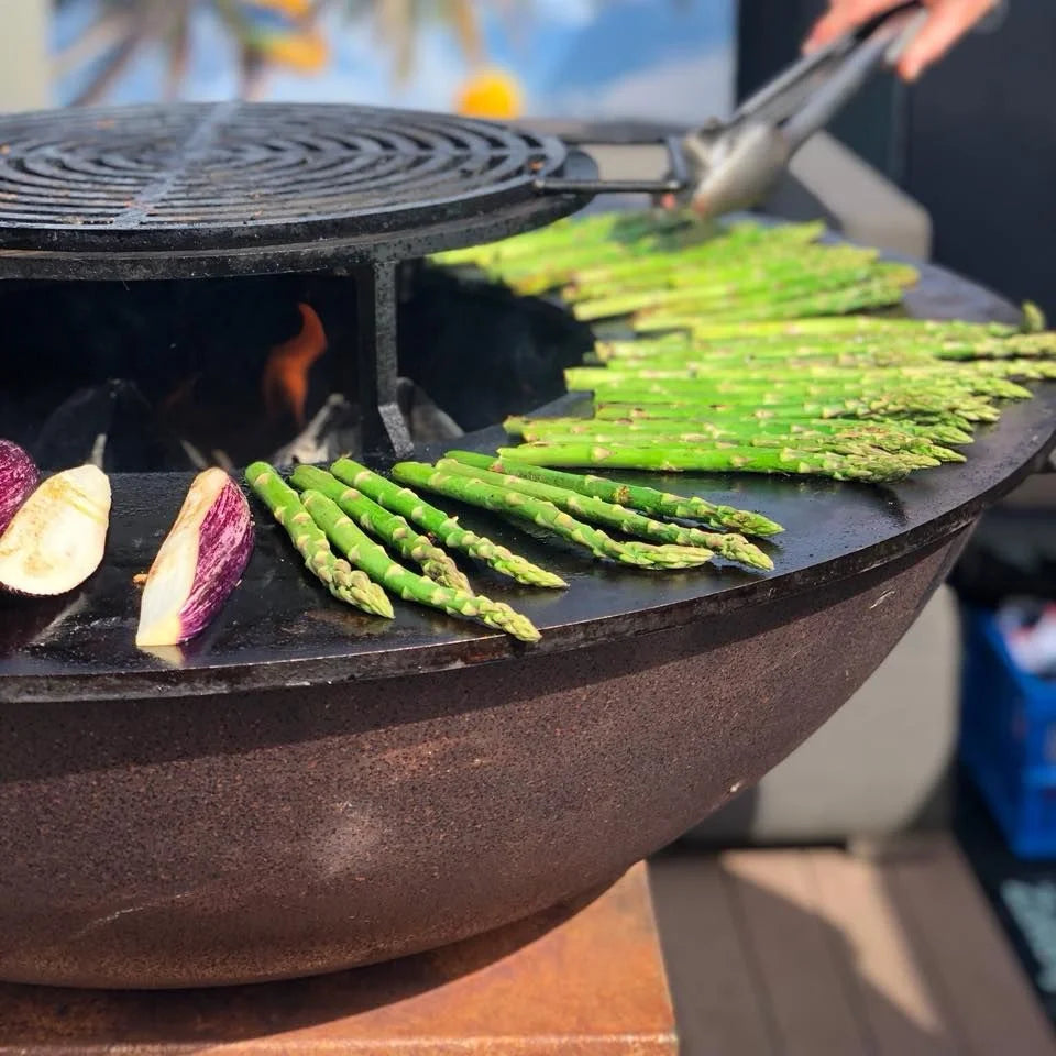 Barbecue extérieur en fonte noire avec des asperges et des aubergines violettes en train de cuire sur sa surface en grille