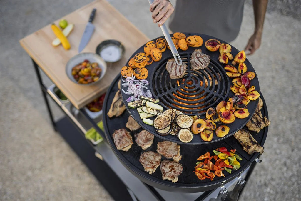Gril rond noir avec des fruits et légumes colorés dessus, conçu pour la cuisson en extérieur.