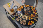Gril rond noir avec des fruits et légumes colorés dessus, conçu pour la cuisson en extérieur.