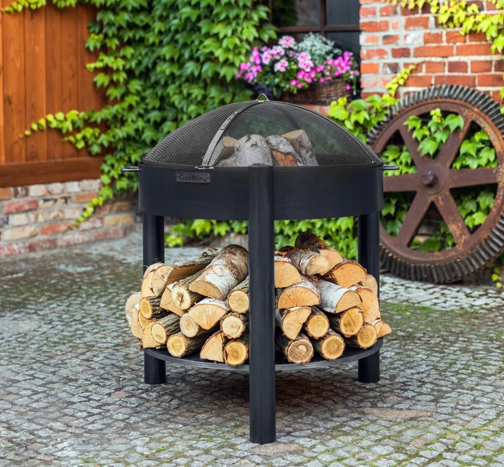 Foyer de feu en métal noir avec couvercle en maille et bûches de bois à l’intérieur.