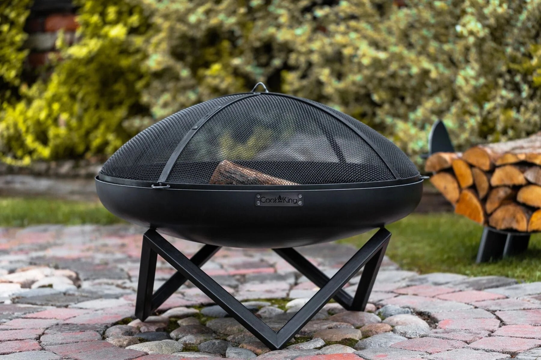 Foyer de feu noir avec un couvercle en filet et un support, conçu pour un usage extérieur.