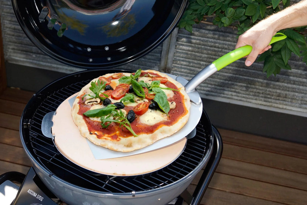 Pierre à pizza avec manche vert et base noire, conçue pour une distribution uniforme de la chaleur sur les grills extérieurs.