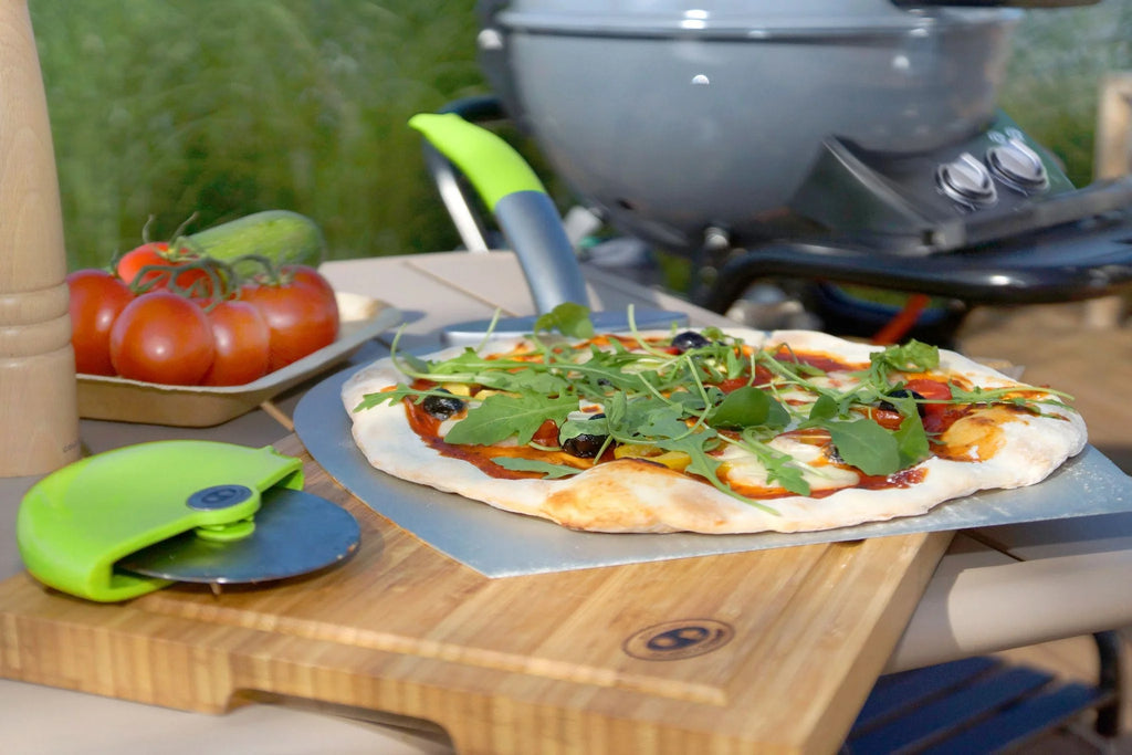 Plateau en pierre à pizza avec poignée verte et base en bois, conçu pour la cuisson en extérieur.