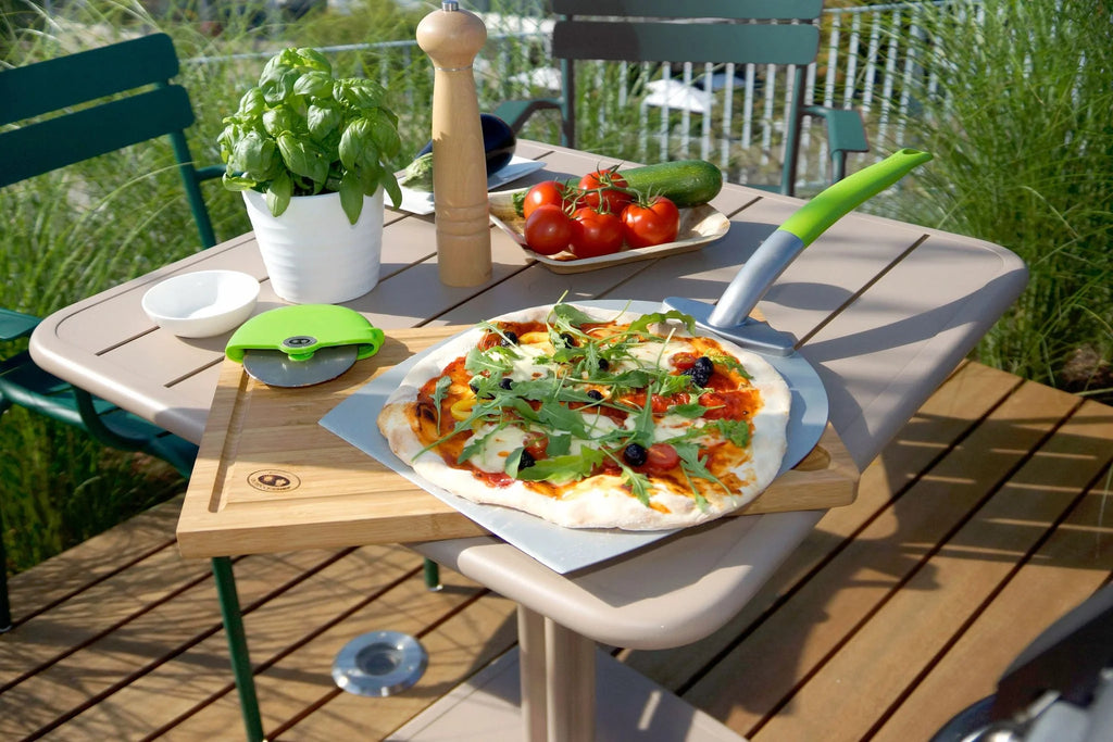 Plateau en pierre à pizza avec poignée verte et base blanche, conçu pour cuire des pizzas dans un four à bois.