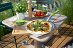 Plateau en pierre à pizza avec poignée verte et base blanche, conçu pour cuire des pizzas dans un four à bois.