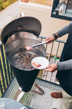 Barbecue au charbon avec un corps cylindrique noir et une grille argentée.