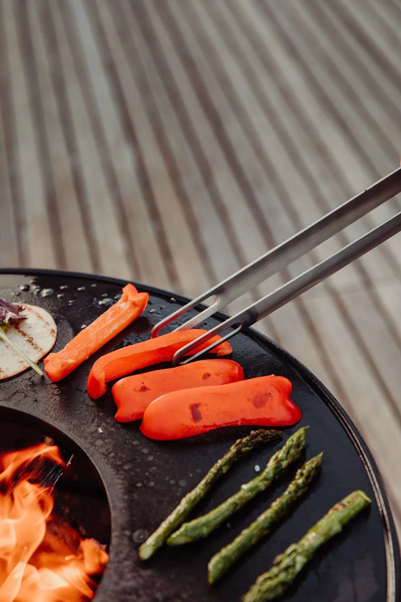 Grilleuse pour pains de hot-dog rouge avec pinces noires et asperges.