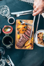 Planche à découper en bois avec steak grillé et légumes, fond vert foncé.