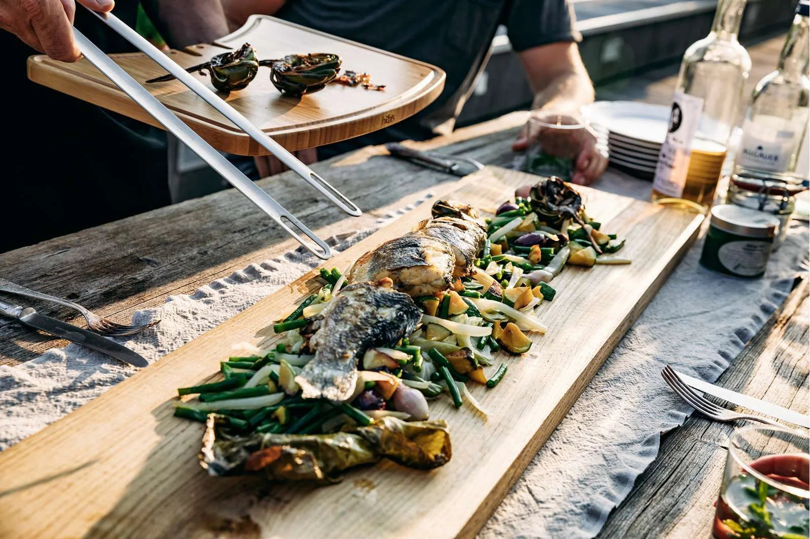 Planche de service en bois avec poisson grillé et légumes.