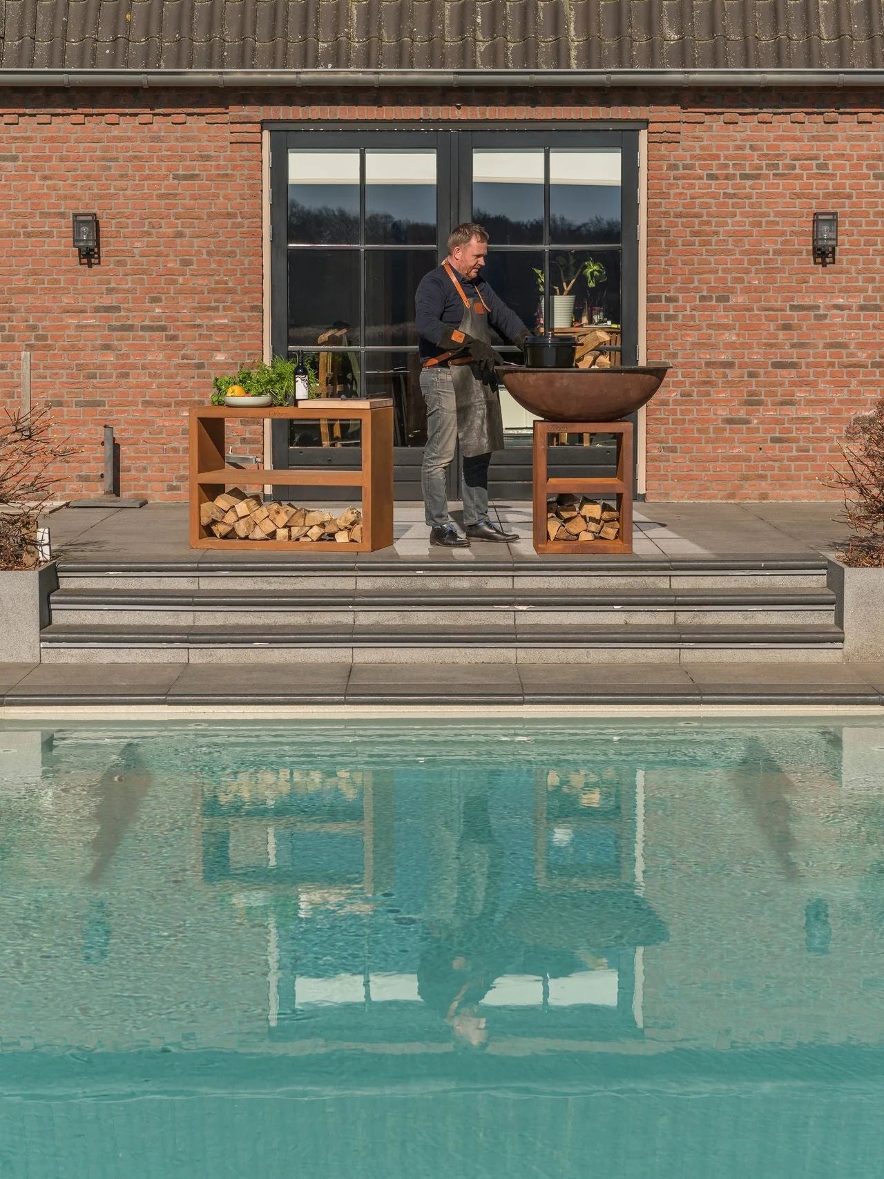 Gril en fonte de couleur cuivre rouillé avec tables latérales en bois et rangement pour bois de chauffage.