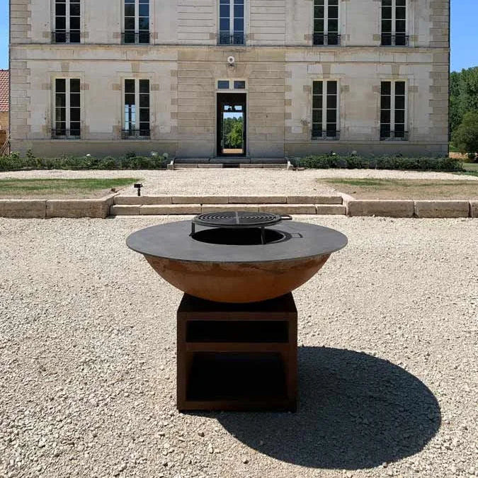 Foyer de feu en forme de bol de couleur rouille avec un insert de gril noir et une base en bois sombre.
