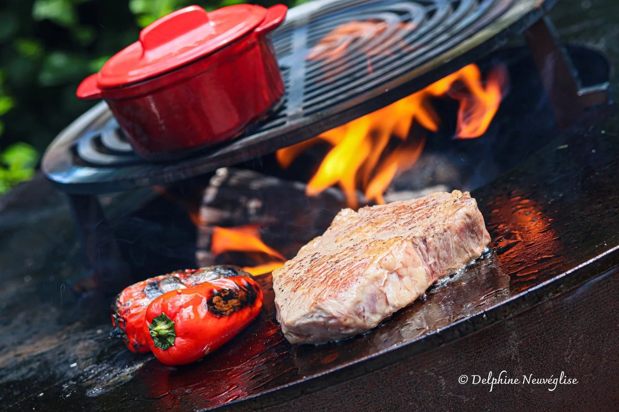 Pot en fonte émaillée rouge avec un couvercle assorti posé sur une grille de gril au-dessus d’une flamme ouverte.
