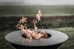 Un foyer de feu métallique circulaire élégant avec un design moderne et des flammes orange lumineuses dansant dans son intérieur sombre.