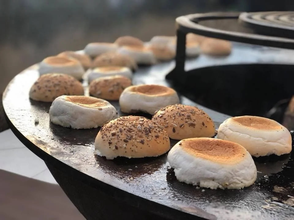 Petits pains grillés dorés-bruns avec des graines de sésame et des sommets de guimauve blanche qui grésillent sur une plaque en fonte noire.