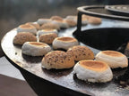 Petits pains grillés dorés-bruns avec des graines de sésame et des sommets de guimauve blanche qui grésillent sur une plaque en fonte noire.