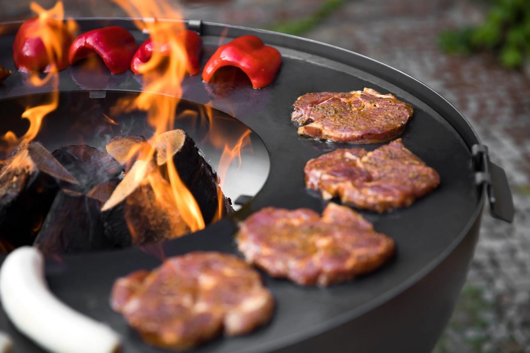 Gril en fonte noire avec des poivrons rouges et des flammes.