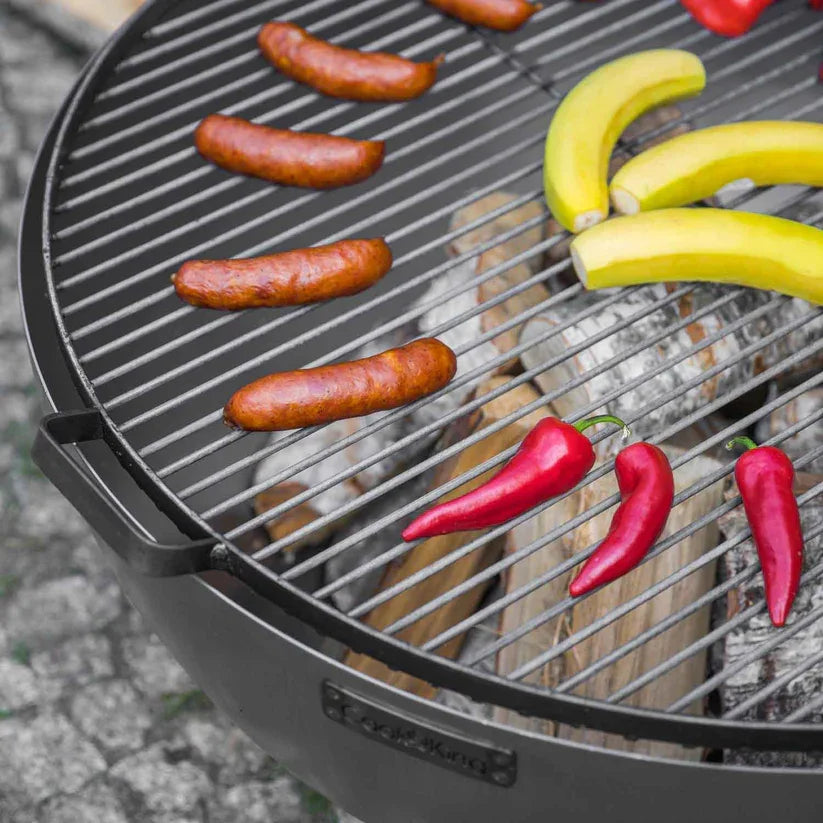 Barbecue au charbon avec des saucisses, des bananes et des poivrons sur la grille.