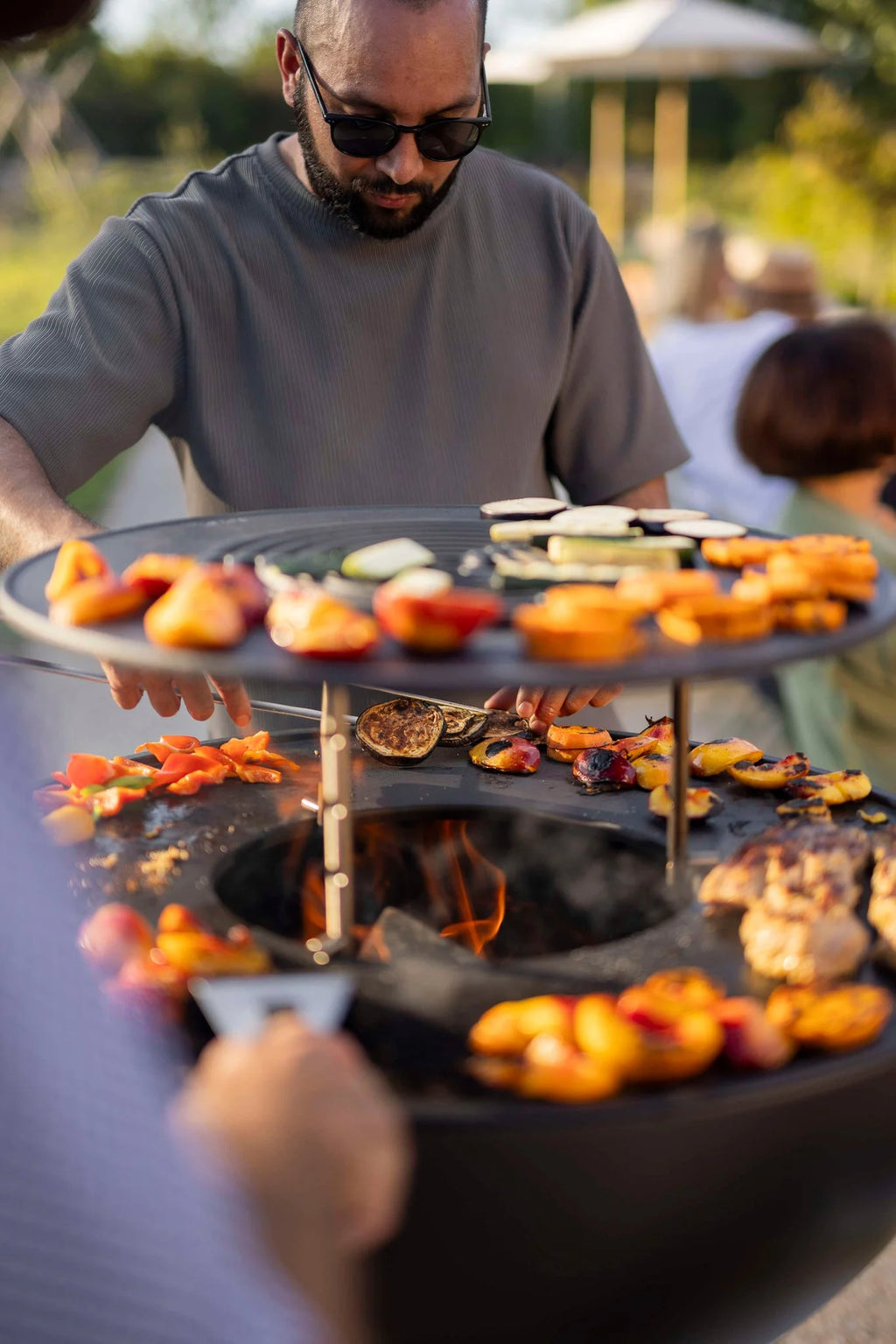 Gril circulaire noir avec poignées en bois et grille en métal, conçu pour la cuisson en extérieur.