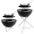 Gril en forme de bol noir avec des pieds en métal et un wok sur le dessus, conçu pour la cuisson en extérieur.