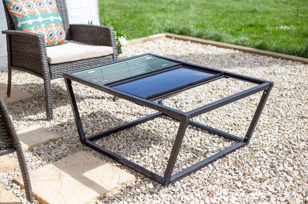 Table basse d’extérieur à cadre en métal noir avec un plateau en verre comportant deux sections distinctes : une claire et une foncée, installée sur une terrasse en gravier.