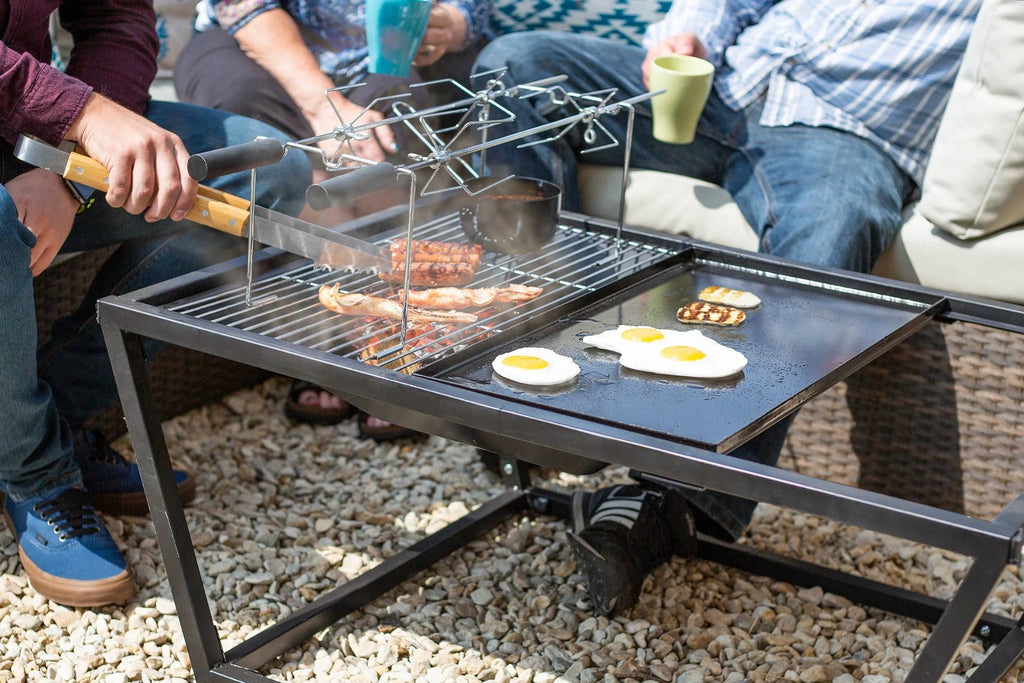 Table de grill extérieur en métal noir avec une surface de plaque chauffante plate et un support supérieur pour brochettes ou petits objets.