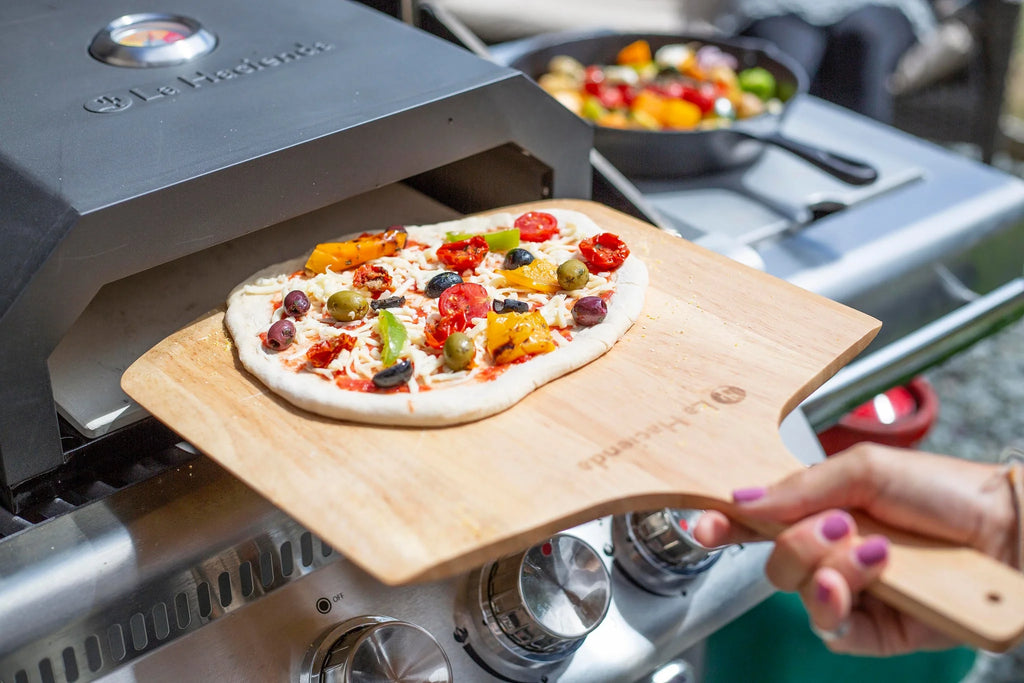 Une palette à pizza en bois avec une finition lisse, brun clair et le logo ’le chef’ gravé près de sa poignée.