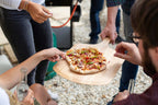 Pelle à pizza en bois avec une pizza pepperoni et légumes fraîchement cuite reposant dessus
